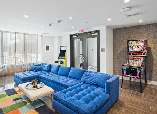 Our lounge and gaming zone with a blue sofa and arcade games at Hollywood Heights on the Boulevard Luxury Apartments in Hollywood, FL
