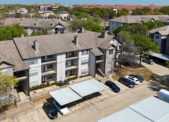 An apartment building with a parking lot and covered parking spots at Jefferson Place Apartments in Irving, TX