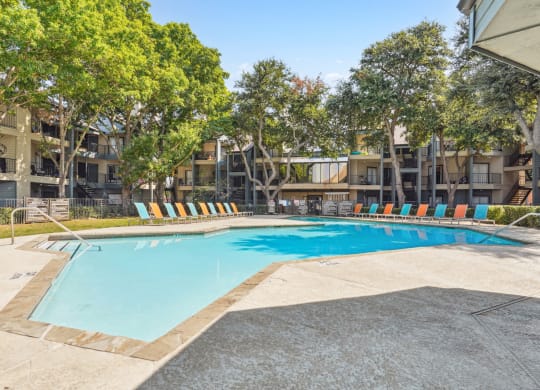 Relaxing pool area with lounge chairs and umbrellas at Laurels of Sendera apartments in Arlington, TX