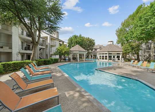 A pool surrounded by lounge chairs and trees.
