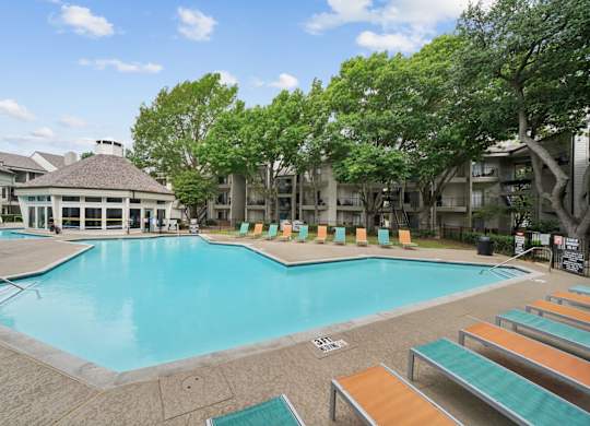A large swimming pool surrounded by sun loungers and trees.