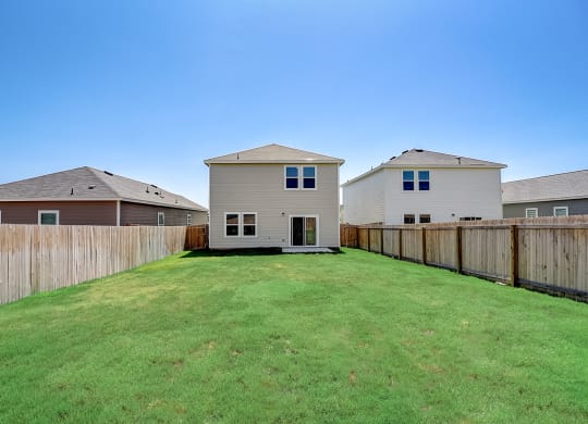 a backyard with a fence and two houses in the background at Beacon at Meridian, San Antonio, TX