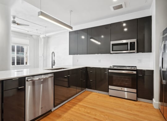 View from inside kitchen with microwave, dishwasher and stove/oven. Black cabinetry provides beautiful contrast to the white countertops. Mid Elm Lofts in Dallas, TX