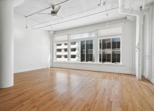 Large living room with polished wood floors, large windows, and a ceiling fan at Mid Elm Lofts in Dallas, TX