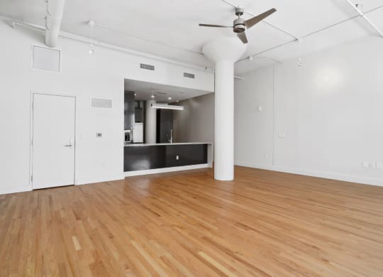 Standing in the living area looking toward the kitchen with a ceiling fan overhead and polished wood floors below at Mid Elm Lofts in Dallas, TX