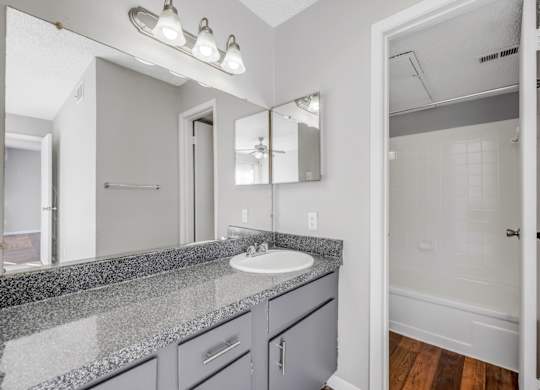 A bathroom with a sink, mirror, and lighting fixture.