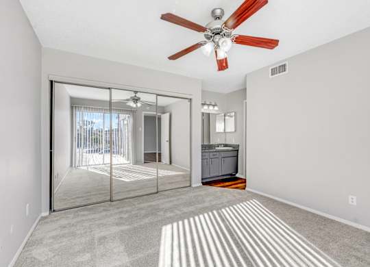 A bedroom with a ceiling fan and a closet with sliding mirrored doors at Montfort Crossing Apartments in Dallas, TX.