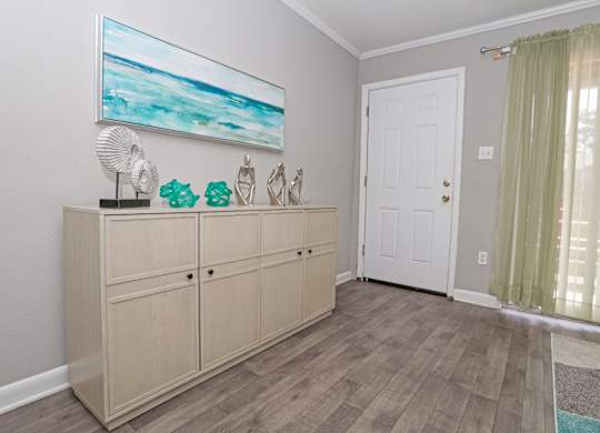 A cypress entrance with a large painting on the wall and wooden cabinet at The Marq in Shreveport, LA