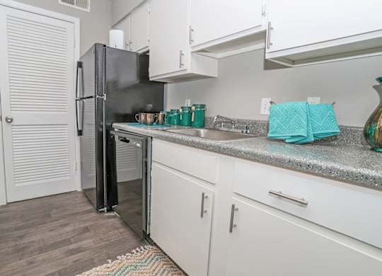 A black refrigerator is in a cypress kitchen with white cabinets at The Marq in Shreveport, LA