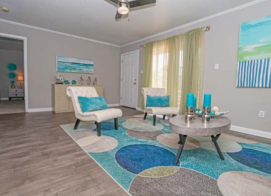 A cypress living room with a blue and white rug, a white chair, and a painting of a beach scene on the wall at The Marq in Shreveport, LA