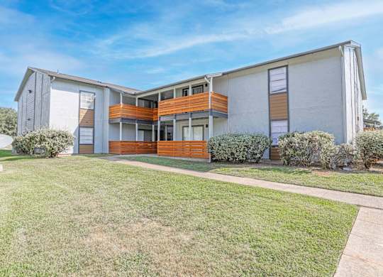 A modern two-story apartment building with a white exterior and a balcony on the second floor and patio on the first floor at The Marq apartments in Shreveport, LA