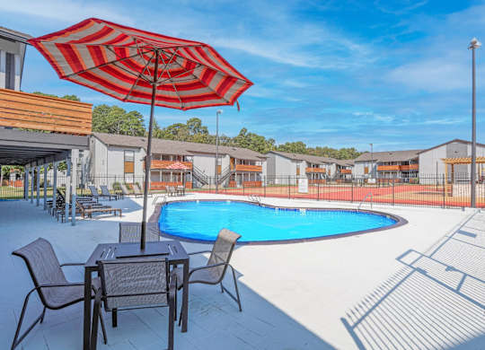 A red and white striped umbrella is over a table with chairs by a pool at The Marq apartments in Shreveport, LA