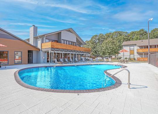 A large outdoor swimming pool surrounded by a patio area with lounge chairs and umbrellas at The Marq apartments in Shreveport, LA