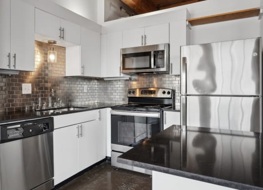 Murray Lofts apartment kitchen with white cabinets, stainless steel appliances and black counter tops | Deep Ellum Lofts in Dallas, TX