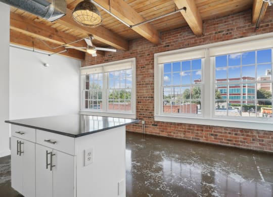 View of kitchen island and living room with brick wall and large windows with scenic view | Deep Ellum Lofts in Dallas, TX