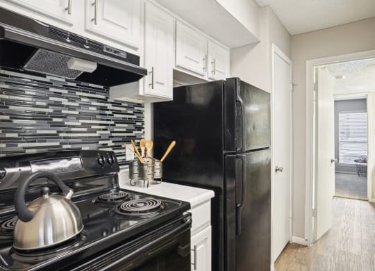 Model A2 floor plan kitchen with black appliances, tile backsplash, and white cabinets Noel on The Parkway in Dallas, TX