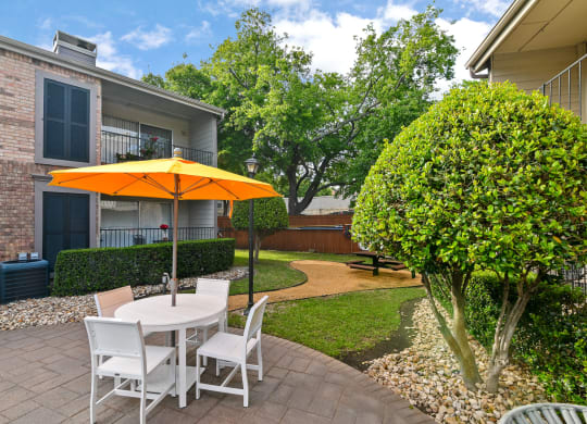 a patio with a white table with an orange umbrella and white chairs