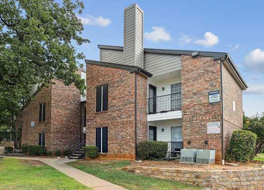 A two-story, brick apartment building with balconies and patios at The Oaks of Denton Apartments in Denton, TX