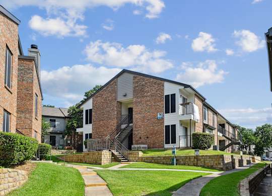An apartment building with green lawns in front at The Oaks of Denton Apartments in Denton, TX