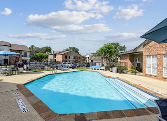 An outdoor swimming pool with apartment buildings in the background at The Oaks of Denton Apartments in Denton, TX