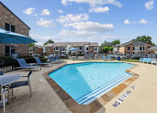 A pool surrounded by comfortable blue lounge chairs at The Oaks of Denton Apartments in Denton, TX