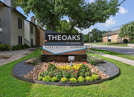 A sign for The Oaks of Denton Apartments is in front of a landscaped area in Denton, TX