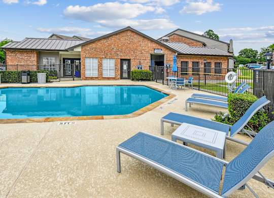 A pool with a blue lounge chair and a brick building in the background.