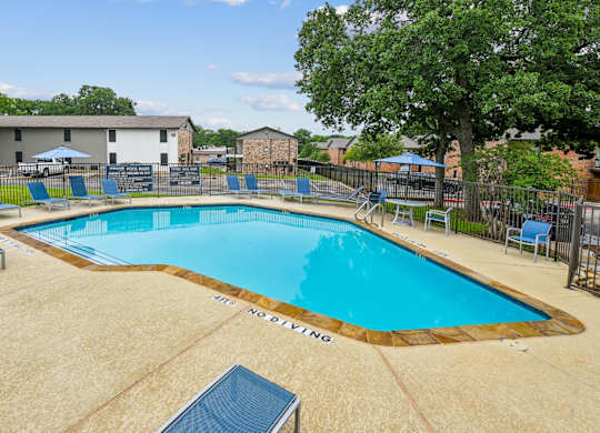 A large swimming pool surrounded by a fence and lounge chairs.