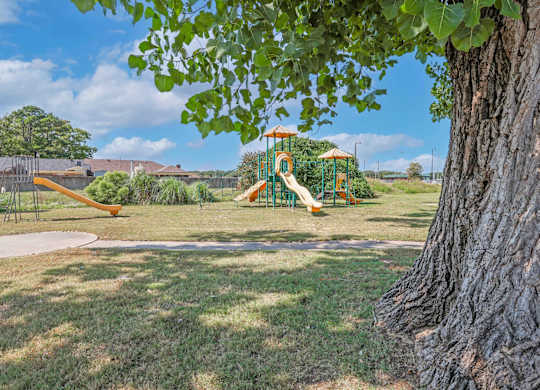 A playground with a slide and a tree in the foreground at Orleans Square in Shreveport, LA