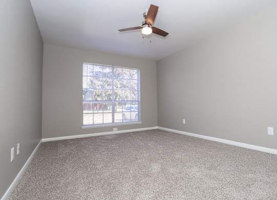 A bedroom with a ceiling fan, large window, and lush carpet at Orleans Square in Shreveport, LA
