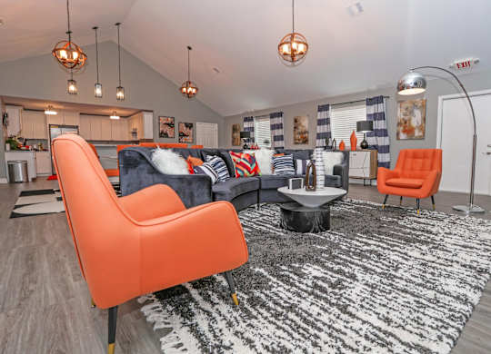 A clubhouse room with a black and white rug, orange chairs, and a kitchen area in the background at Orleans Square in Shreveport, LA