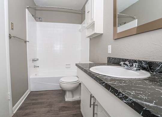 A bathroom with a marble counter, toilet, sink, and tub at Orleans Square in Shreveport, LA
