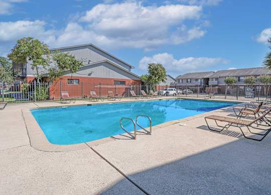 A swimming pool with chairs, a ladder, and apartment buildings in the background at Orleans Square in Shreveport, LA