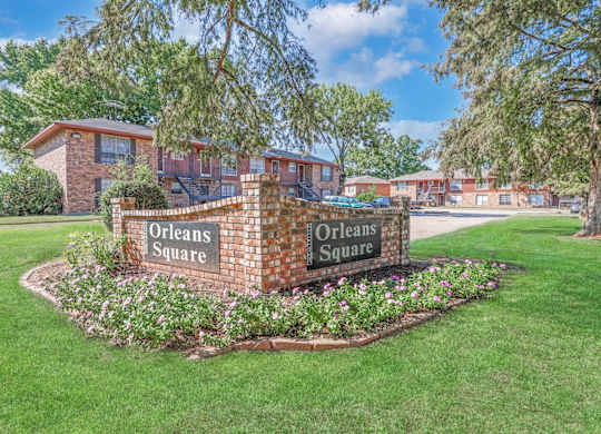A brick sign that reads "Orleans Square" is surrounded by flowers and greenery at Orleans Square in Shreveport, LA
