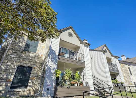 Looking up at our apartment buildings with a balcony and a stone facade at On the Green apartments in Austin, TX