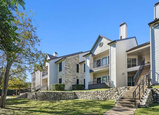 Our modern apartment buildings with a stone wall and a staircase at On the Green apartments in Austin, TX