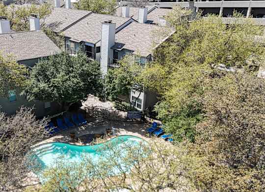 A swimming pool surrounded by lush trees and apartment buildings at The Park on Preston Apartments in Dallas, TX