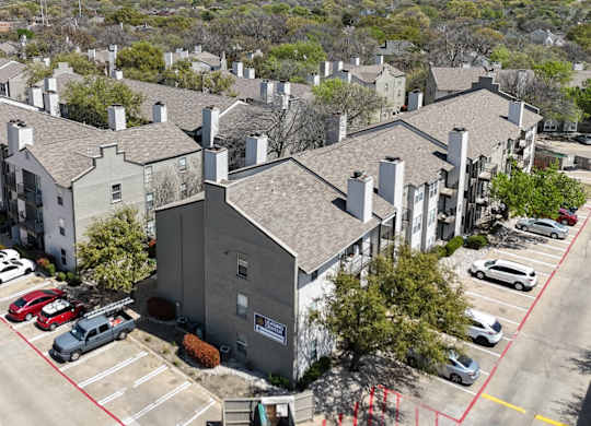 An aerial view of an apartment complex with parking and a dumpster at The Park on Preston Apartments in Dallas, TX