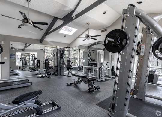 A gym with a variety of equipment including a weight bench, a barbell, and a squat rack at Preston Oaks Apartments in Dallas, TX.