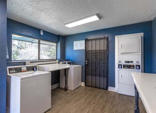 A laundry facility with washers, dryers, and a white folding table at Preston Oaks Apartments in Dallas, TX.