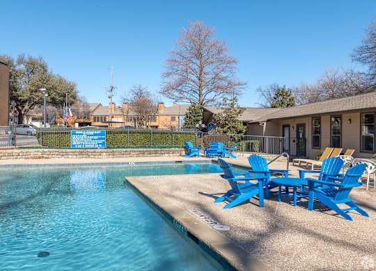 A pool with blue chairs a blue sky in the background at Preston Oaks Apartments in Dallas, TX.