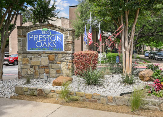 An entry sign in front of a stone building at Preston Oaks Apartments in Dallas, TX.