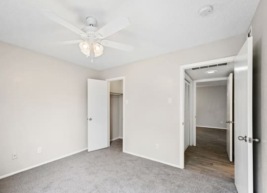 a bedroom with a ceiling fan and a hallway in the background