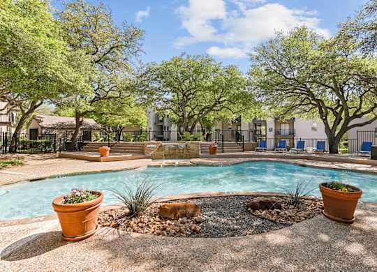A pool surrounded by trees and potted plants.