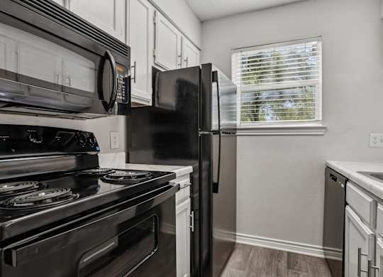 A black refrigerator in a kitchen with white cabinets.