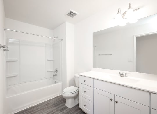a bathroom with white cabinets and a white toilet next to a white bathtub at Beacon at Meridian, San Antonio
