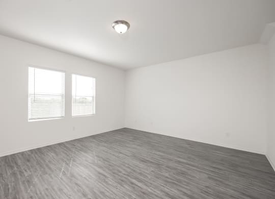 an empty bedroom with two windows and a hardwood floor at Beacon at Meridian, San Antonio, TX