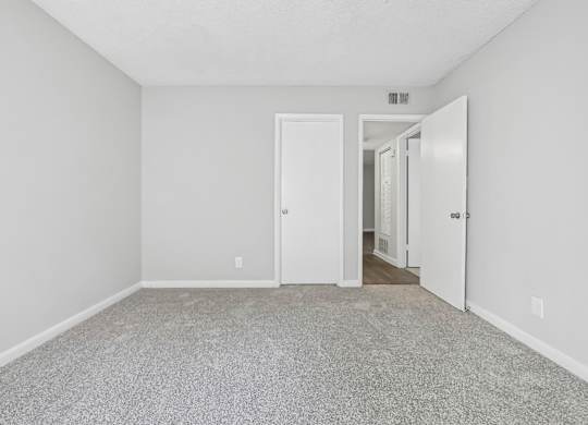 First bedroom with a carpeted floor and a closet door in B1 floor plan at Riverwood Crossing apartments in Roswell, GA.