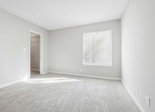 First bedroom with a carpeted floor, a window with blinds, and walk-in closet in the B1 floor plan at Riverwood Crossing apartments in Roswell, GA..