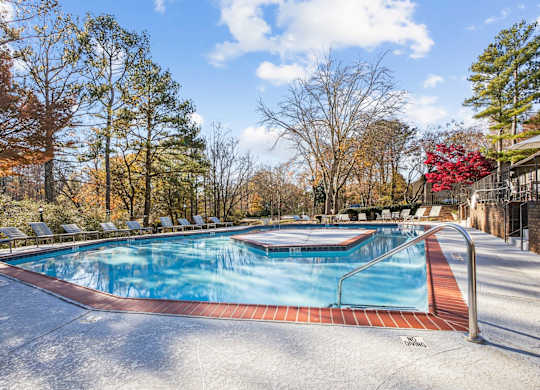 A pool surrounded by trees in a sunny day at Riverwood Crossing apartments in Roswell, GA.
